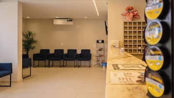 A reception area with a counter, chairs, a potted plant, and a wall-mounted shelf with items.
