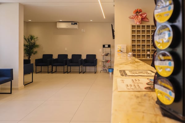 A reception area with a counter, chairs, a potted plant, and a wall-mounted shelf with items. - Hanna Amsterdam Hotel & Eventos (Florianópolis)