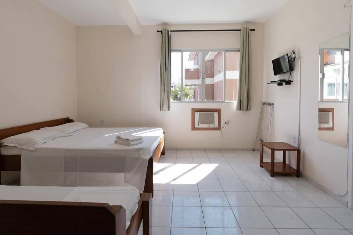 A hotel room with two beds, a TV mounted on the wall, and a window with curtains.