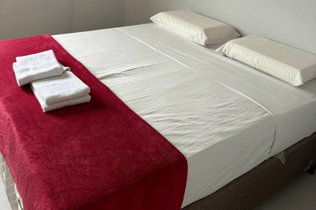 A single bed with white bedding, a red blanket, and two white towels on the side.