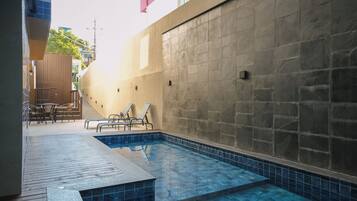 A swimming pool with a tiled deck, lounge chairs, and a stone wall.