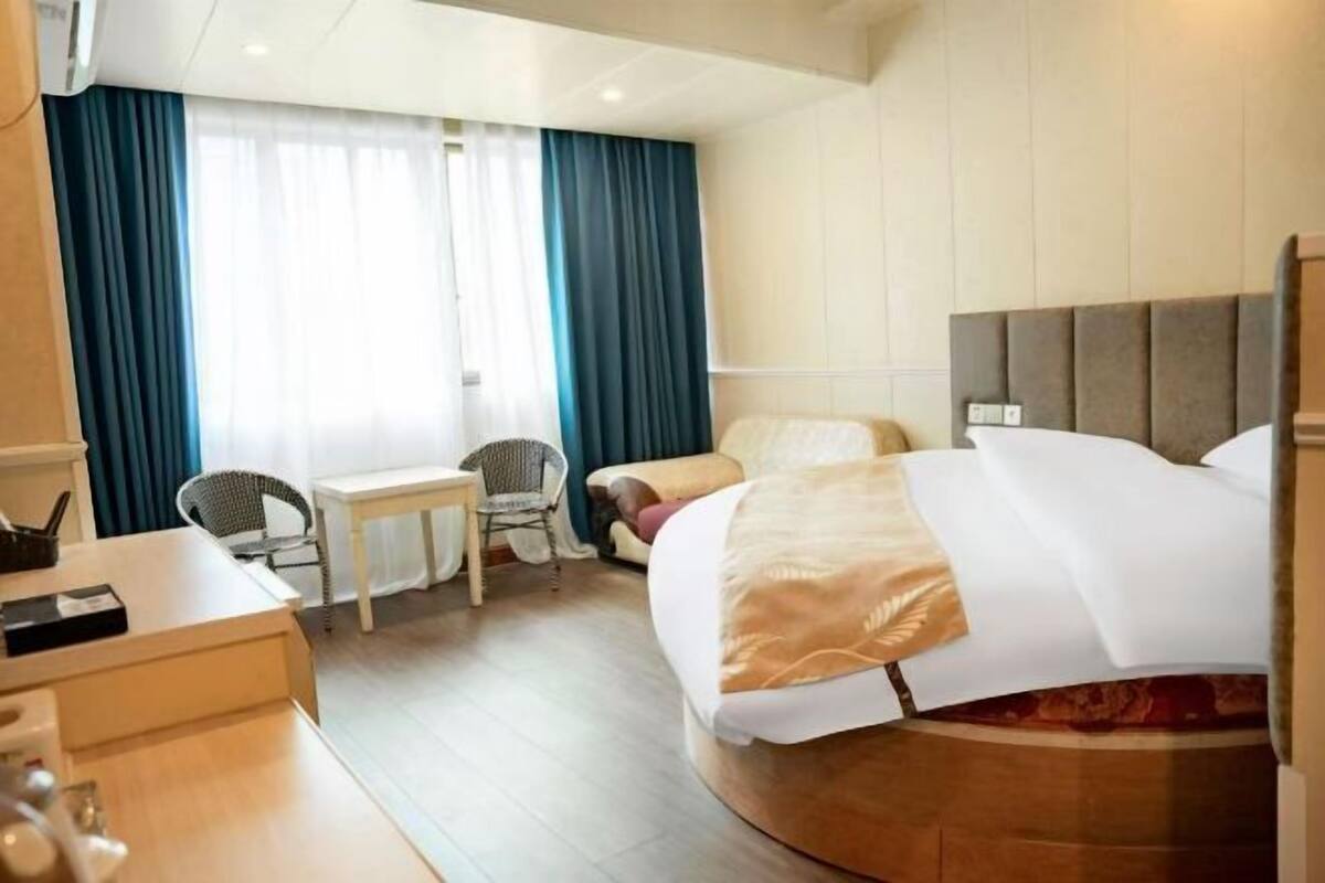 Una habitación de hotel con una cama, un escritorio, una silla y un ventanal con cortinas.