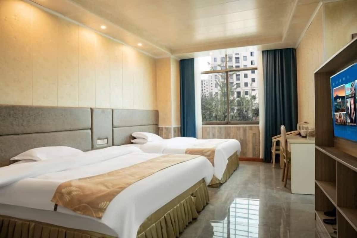 Habitación de hotel con dos camas, televisión, escritorio y vistas a edificios.