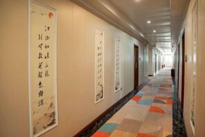 A hotel corridor with a patterned carpet, framed calligraphy on the walls, and doors leading to rooms.