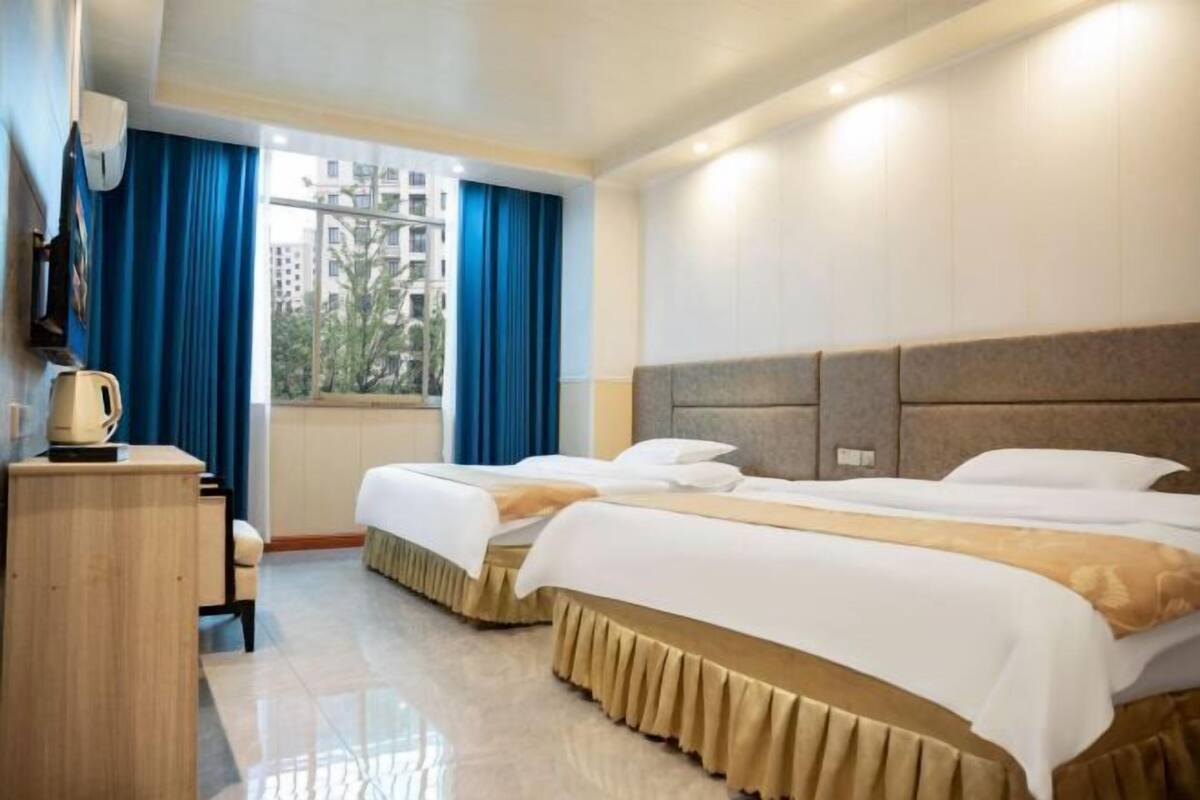 Una habitación de hotel con dos camas, un escritorio, una silla y una ventana con cortinas.