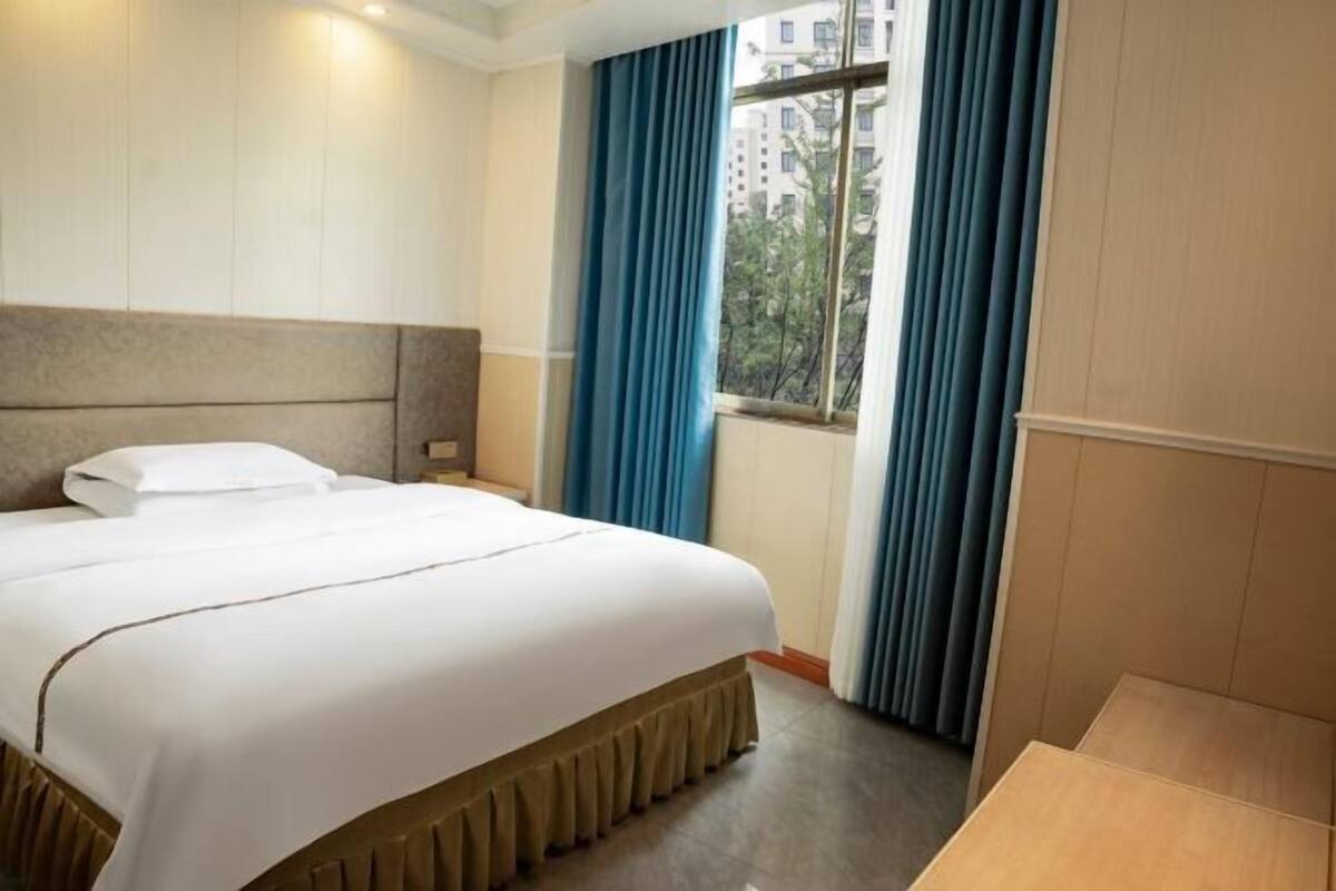 Una habitación de hotel con una cama, una ventana con cortinas y vistas a edificios.