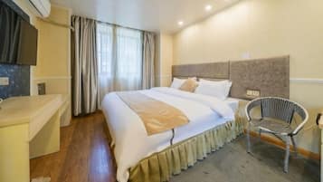 A hotel room with a bed, a chair, a desk, and an air conditioning unit.