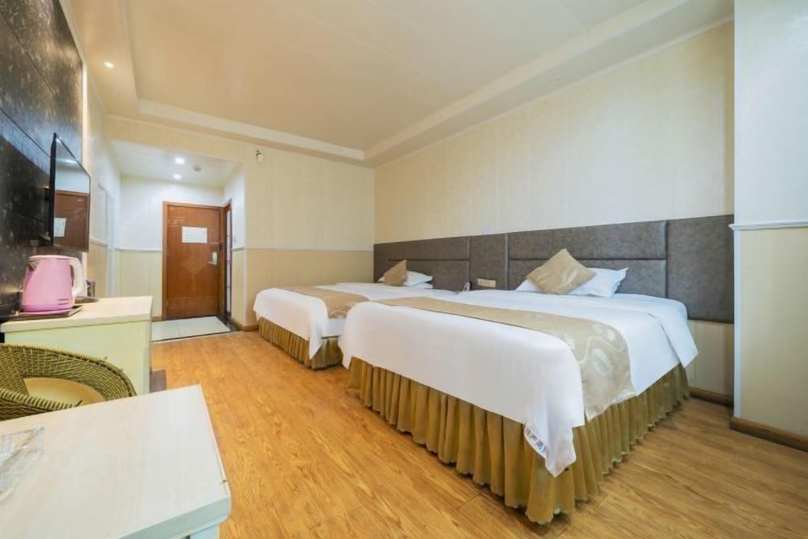 A hotel room with two beds, a wooden floor, a desk with a pink kettle, and a large mirror.