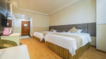 A hotel room with two beds, a wooden floor, a desk with a pink kettle, and a large mirror.