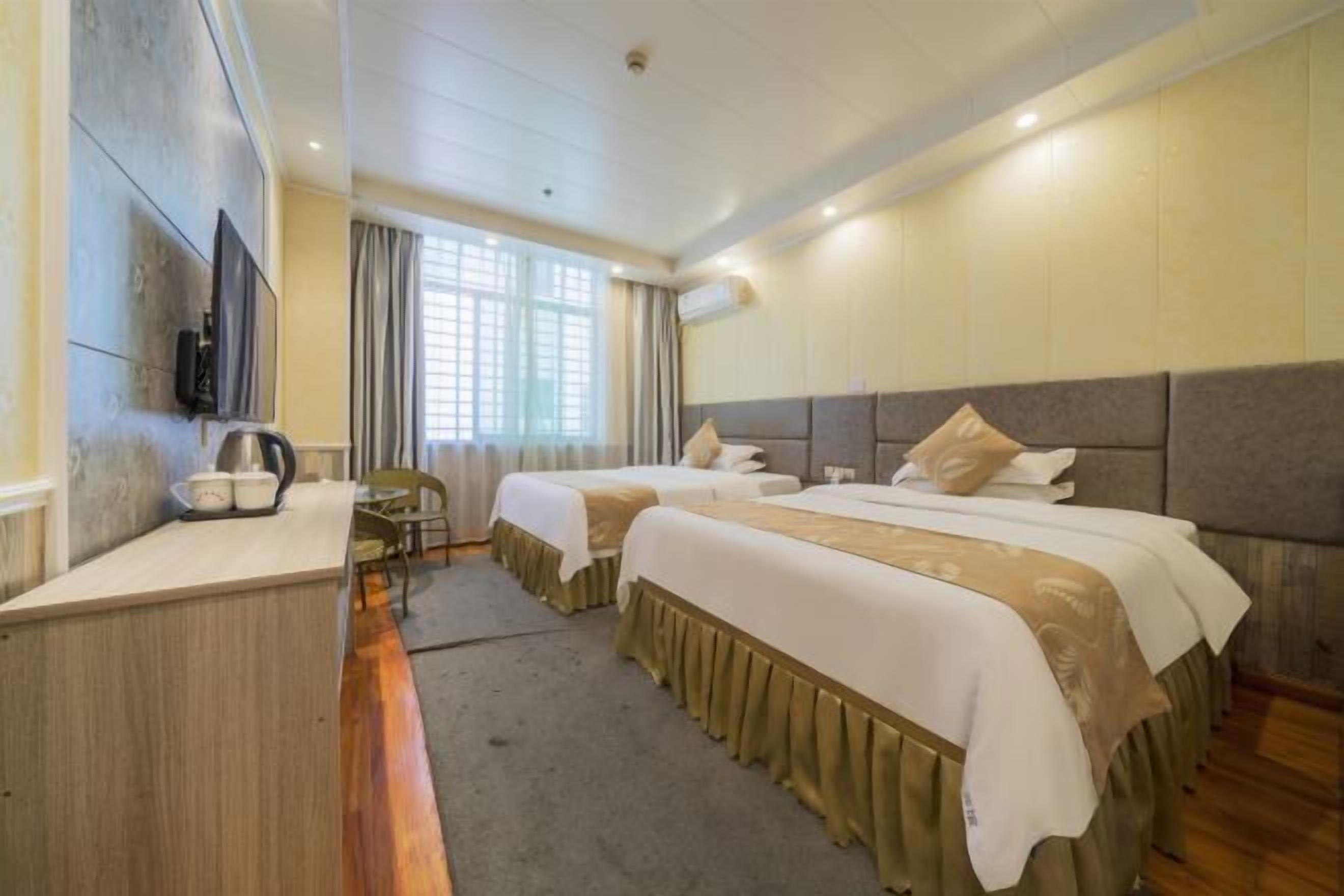 A hotel room with two beds, a desk, a TV, and a window with curtains.