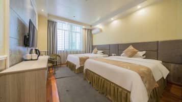 A hotel room with two beds, a desk, a TV, and a window with curtains.