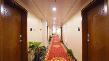 A hotel hallway with a red carpet, wooden doors, and potted plants.