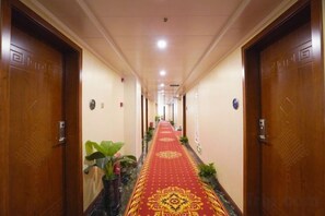 Un pasillo de hotel con alfombra roja, puertas de madera y plantas en macetas.