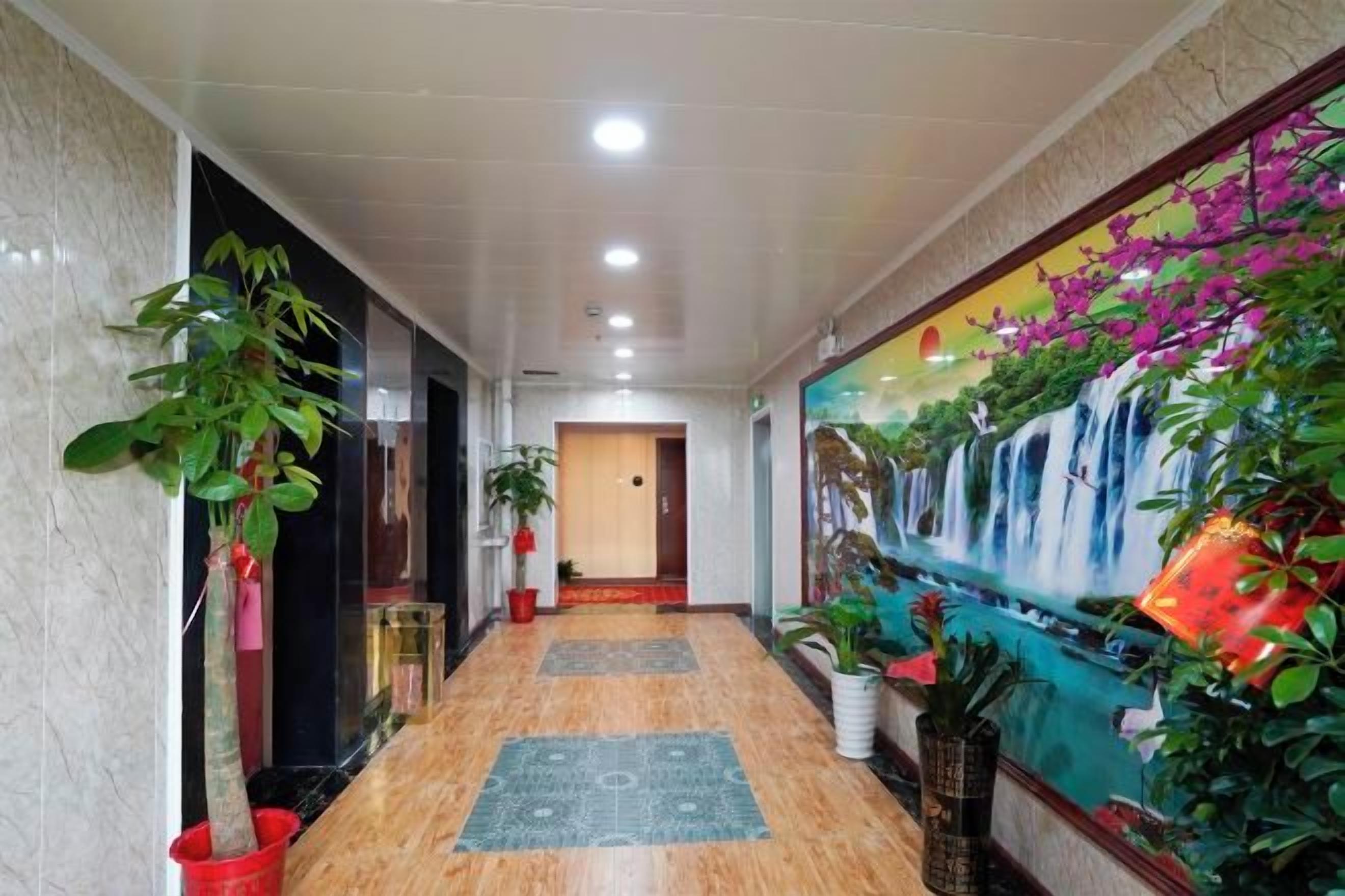 A hotel hallway with a marble floor, potted plants, a mural, and a door at the end.