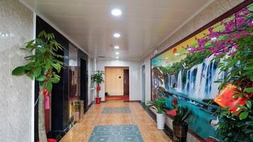 A hotel hallway with a marble floor, potted plants, a mural, and a door at the end.