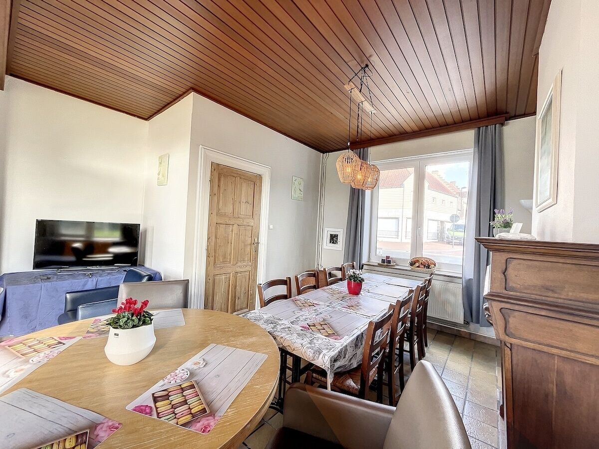Een eetgedeelte met een houten tafel, stoelen en een televisie op de achtergrond.