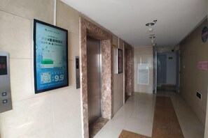 Un corridoio d'albergo con un poster, un ascensore e una porta.