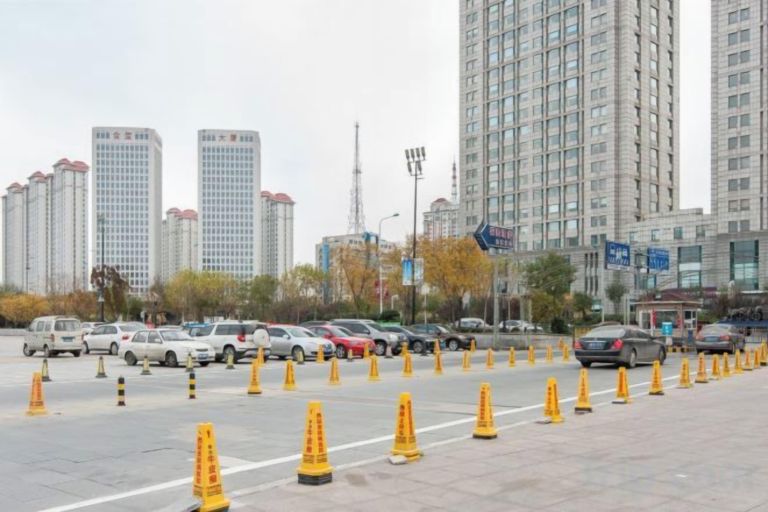 A parking lot with multiple cars and yellow traffic cones, surrounded by tall buildings.
