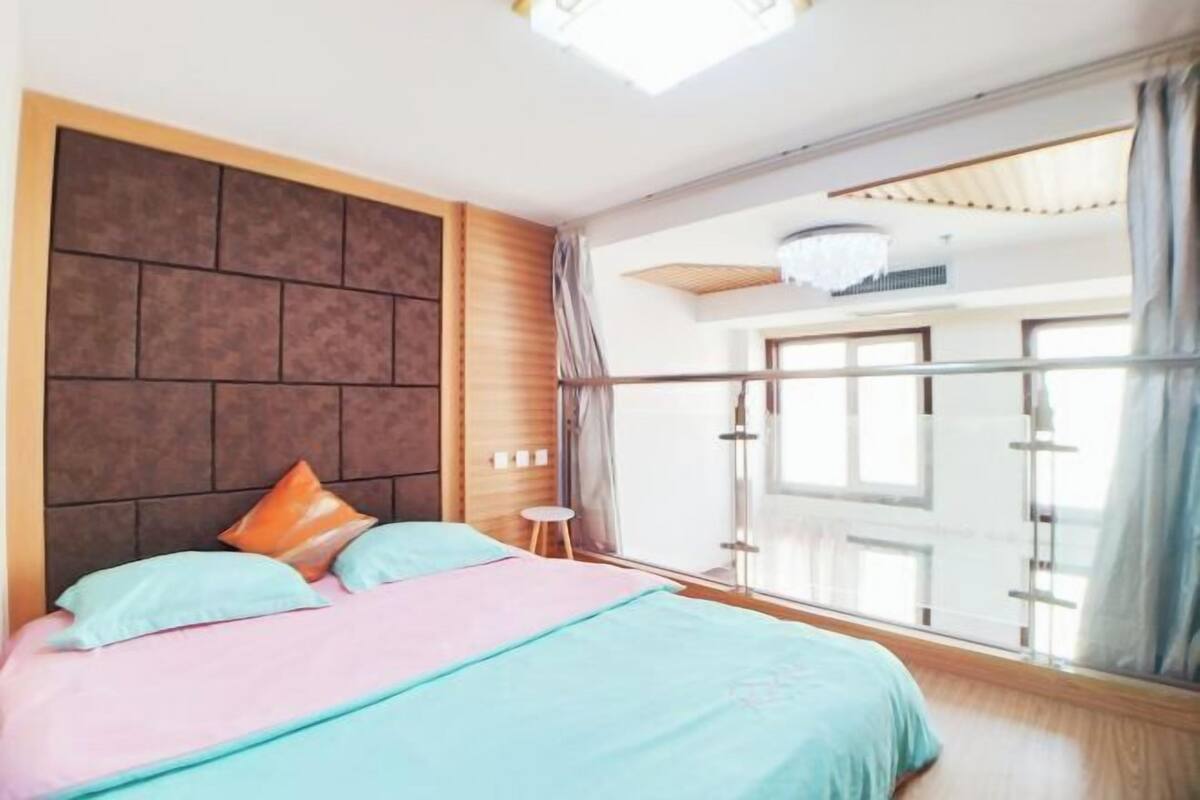 Een slaapkamer met een bed, een klein krukje, een raam met gordijnen en een kroonluchter.