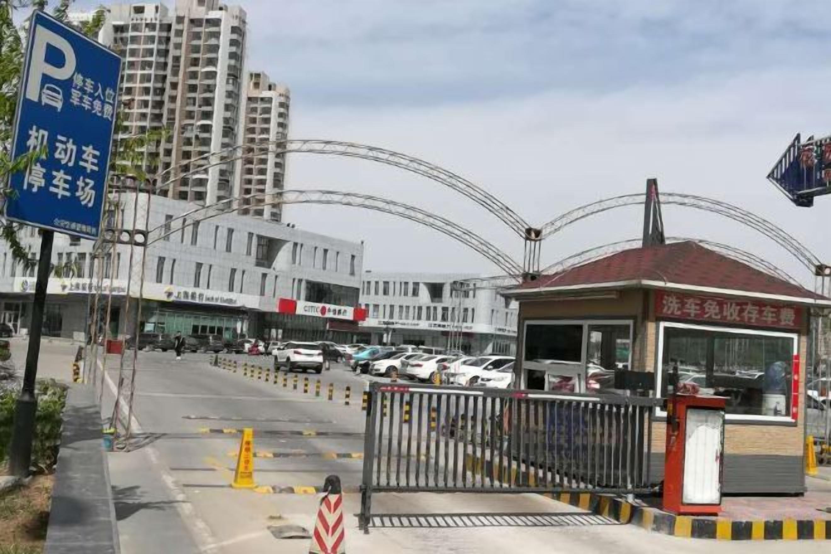 Un espace de stationnement doté d’une entrée avec barrière, d’un guichet et, au fond, d’un bâtiment à plusieurs étages.
