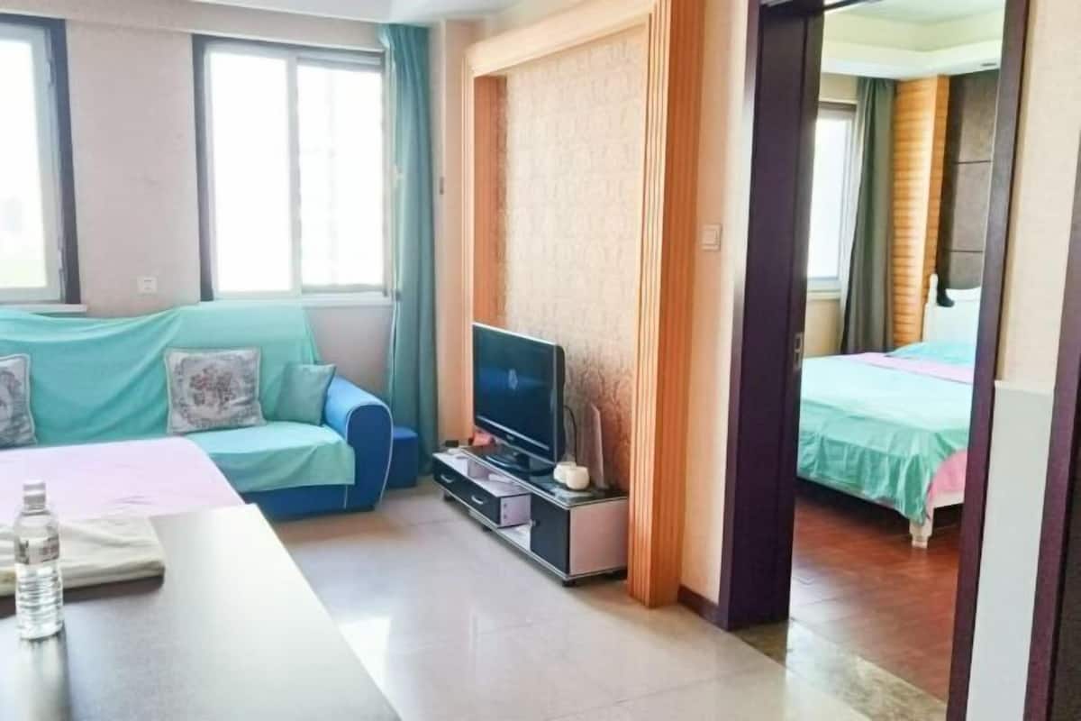Een hotelkamer met een bank, een televisie op een standaard, een bed en een bureau met een waterfles.