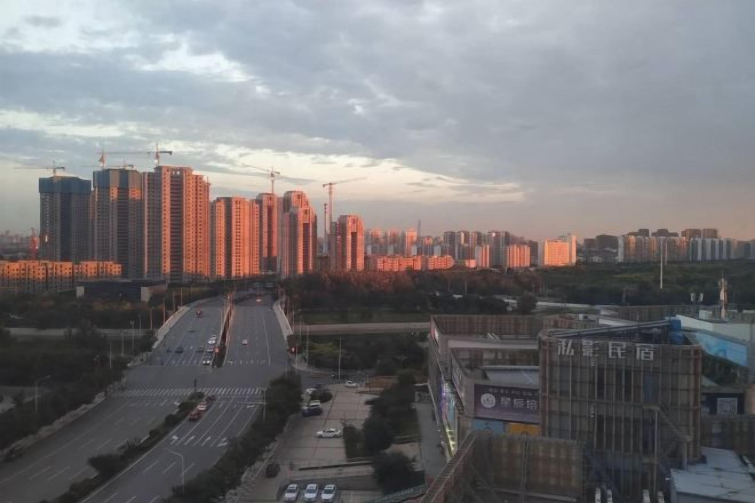 A cityscape with high-rise buildings, a multi-lane road, and a construction crane.