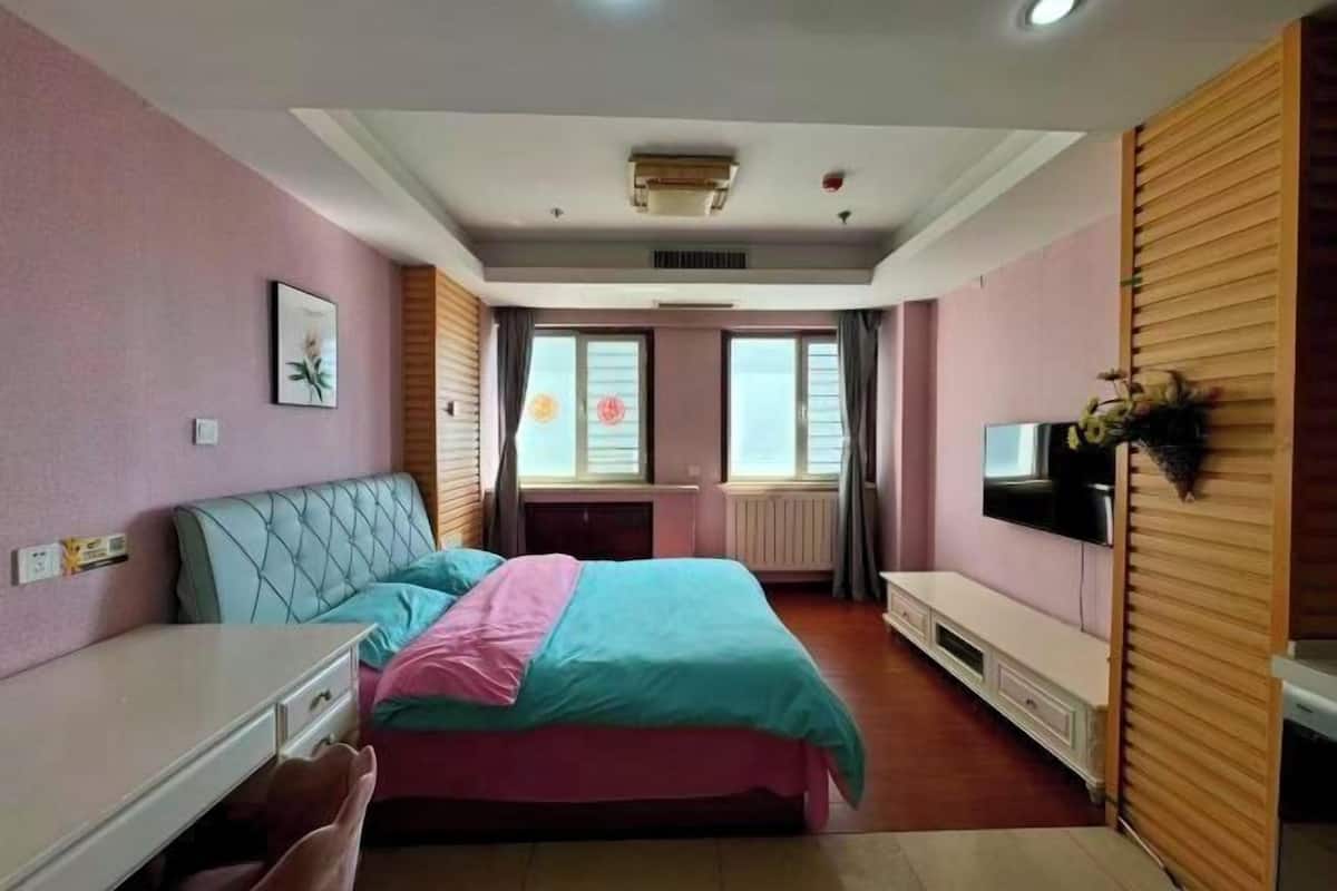 Een slaapkamer met een bed, bureau, televisie en raam.