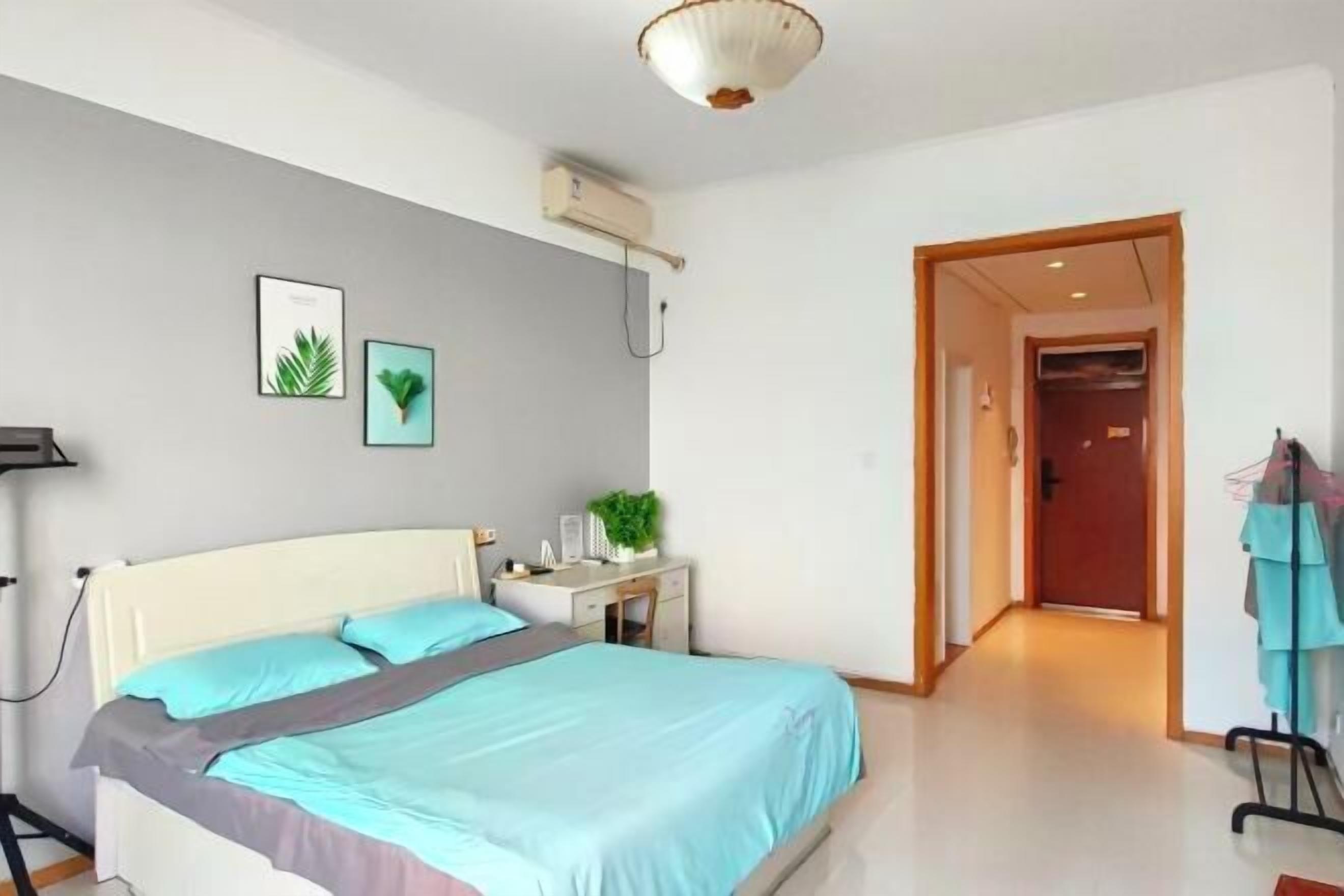 A bedroom with a bed, bedside table, wall-mounted air conditioner, and a door leading to another room.