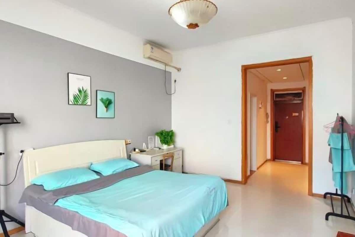 Een slaapkamer met een bed, nachtkastje, wandgemonteerde airconditioner en een deur naar een andere kamer.