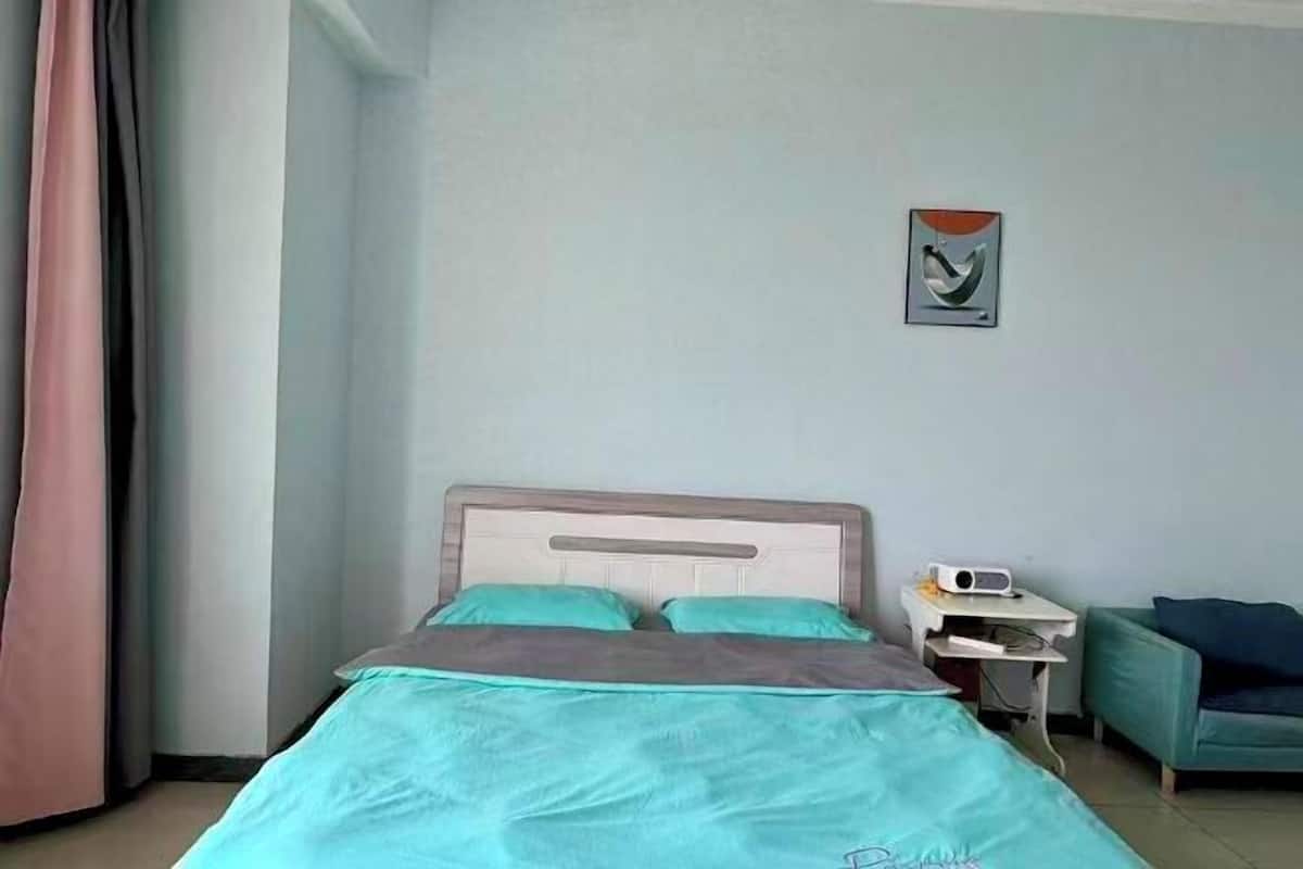 Een hotelkamer met een bed, nachtkastje, stoel en een schilderij aan de muur.
