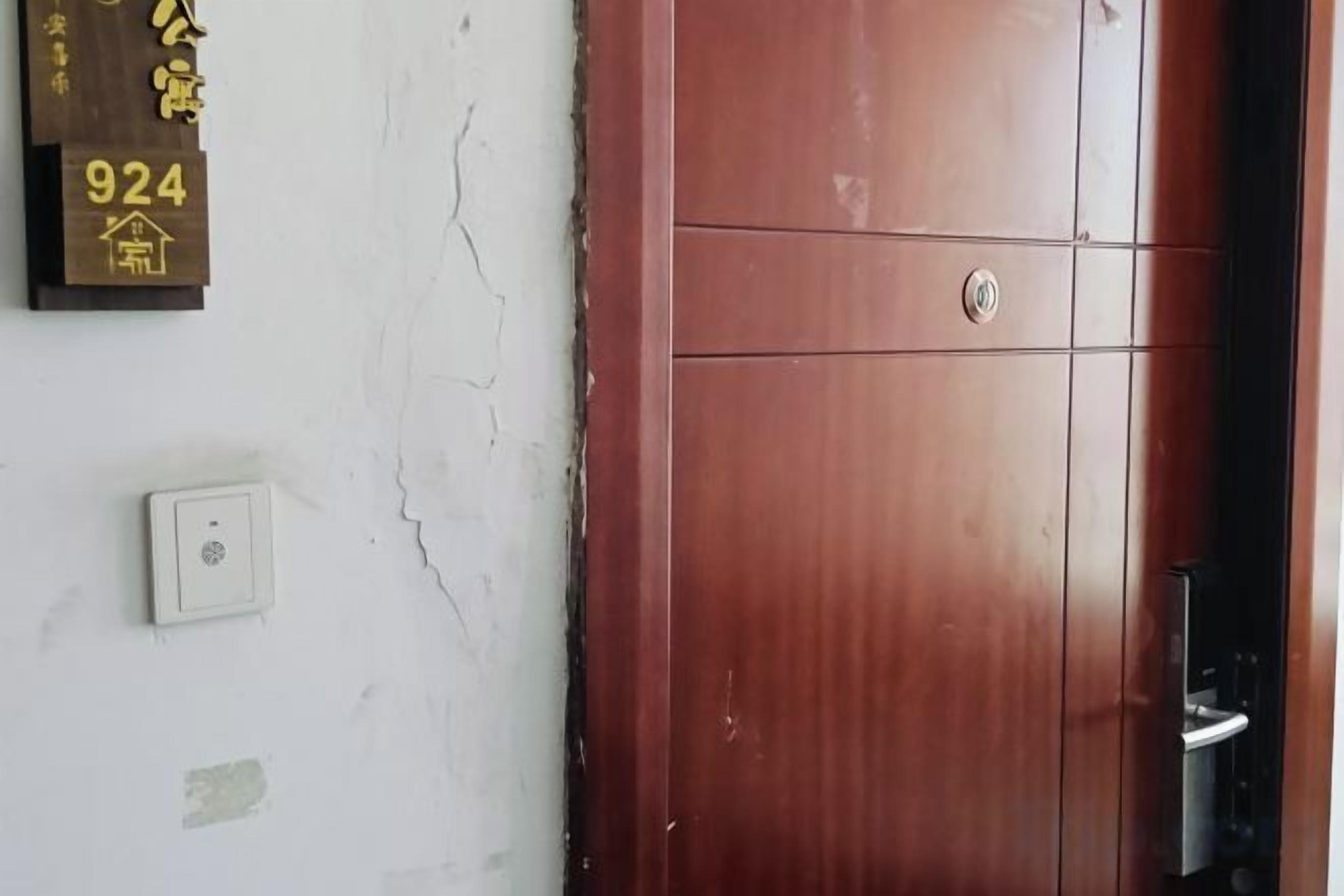 A wooden door with a handle and a keyhole, a wall-mounted light switch, and a plaque with numbers.