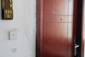 Una puerta de madera con manija y cerradura, un interruptor de luz en la pared y una placa con números.