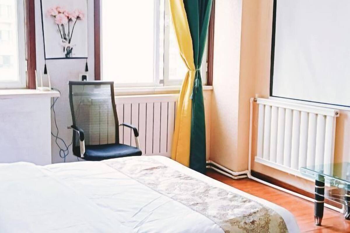 Een hotelkamer met een bed, een stoel, een radiator en een raam met gordijnen.