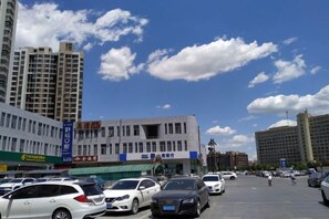 Un estacionamiento con varios autos, un edificio con señalización y un cielo despejado con nubes.