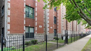 Una hilera de edificios de apartamentos de ladrillo con ventanas numeradas, una valla de metal negro y una acera.