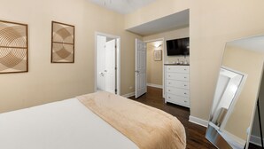 Un dormitorio con cama, cómoda, televisor y dos puertas que dan a otras habitaciones.