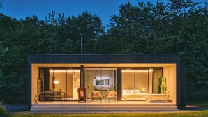 A modern, well-lit house with a spacious patio, a fireplace, and a large window overlooking a garden.