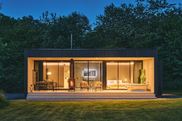 A modern, well-lit house with a spacious patio, a fireplace, and a large window overlooking a garden.