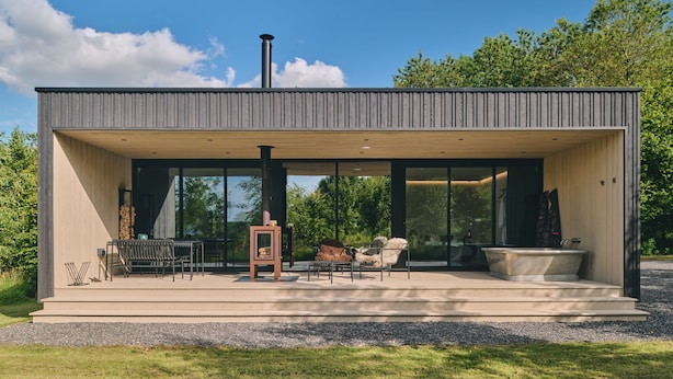 Uma casa moderna com varanda coberta, área de estar externa e uma grande janela com vista para um jardim.