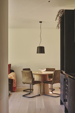 A dining area with a round table, four chairs, a hanging light fixture, and a wooden floor. - Whispering Leaves - Luxury Cottages (Glastonbury)