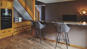 Een keuken met een houten trap, een marmeren aanrecht en twee barstoelen.