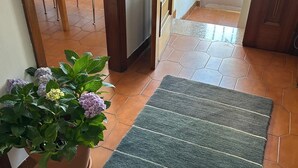 Un pasillo con una planta en maceta, un tapete a rayas y una puerta que da a una habitación con suelo de baldosas.