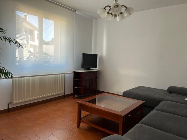 Un salon avec un canapé, une table basse en bois, un téléviseur posé sur un meuble et un radiateur.