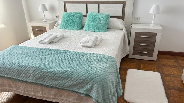 Un dormitorio ordenado con una cama, dos mesitas de noche, una mesilla auxiliar y un reposapiés a juego.