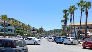 A parking lot with several cars, palm trees, and buildings in the background. - Almirida Paradise Apartments (Chania)