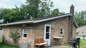 A small stone house with a front porch, a bench, a grill, and a portable air conditioning unit. - Rustic cottage by the mighty Elk! (Girard)