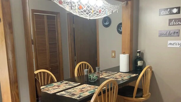 A dining area with a wooden table, four chairs, a hanging light fixture, and a wall with decorative plates and a bottle. - Rustic cottage by the mighty Elk! (Girard)