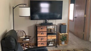 A living room with a black sofa, a flat-screen TV, a wooden cabinet, a lamp, and a patterned rug. - Rustic cottage by the mighty Elk! (Girard)