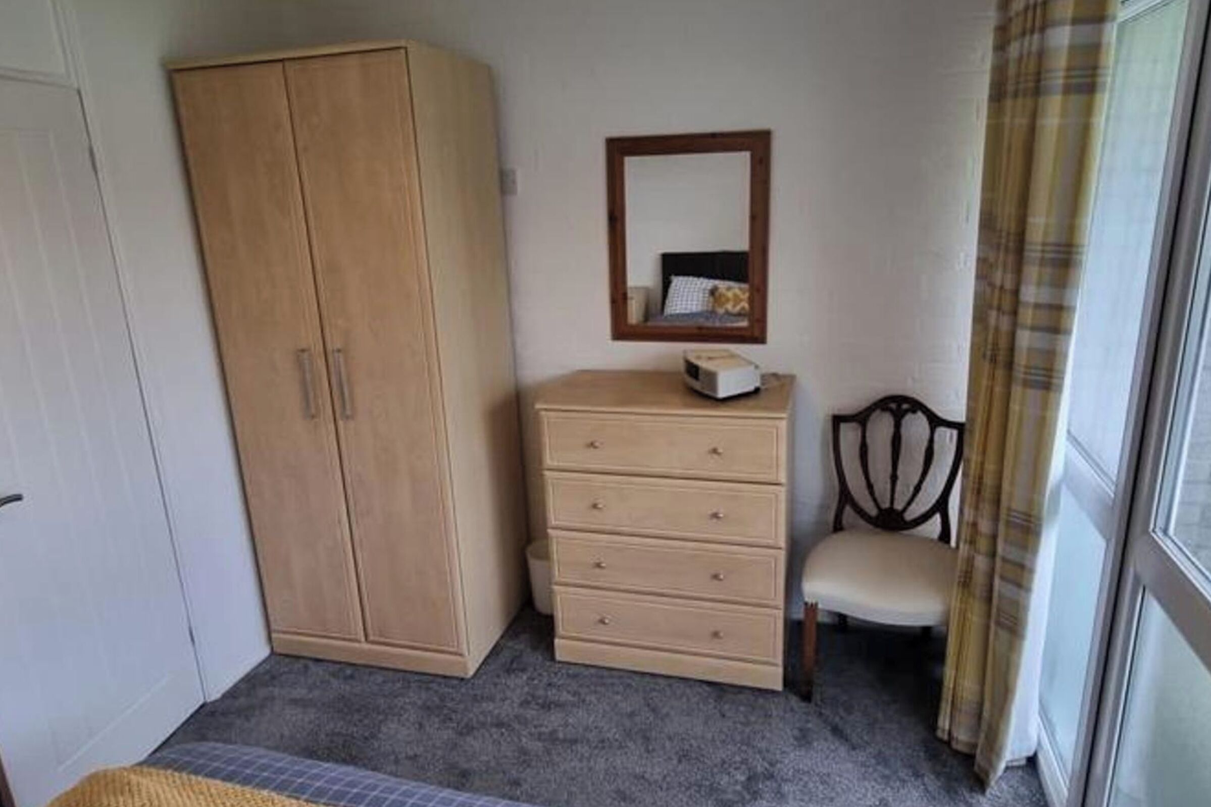 A bedroom with a wardrobe, a chest of drawers, a chair, and a bed.