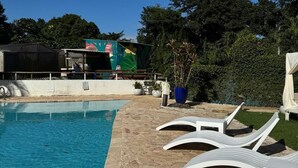 Ein Schwimmbecken mit Liegestühlen, ein überdachter Bereich mit einem farbenfrohen Wandgemälde und üppiges Grün im Hintergrund.